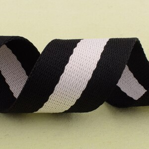 May include: Black and white striped webbing ribbon. The ribbon is woven with a textured pattern.