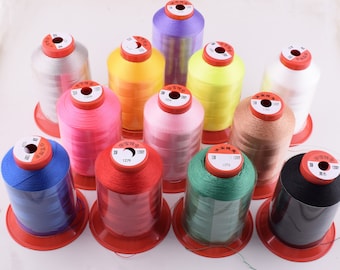 Könnte beinhalten: Sortiment von 12 Garnrollen in verschiedenen Farben, darunter Rot, Rosa, Blau, Grün, Gelb, Weiß, Schwarz und Lila. Jede Rolle ist mit einer Nummer und dem Text "304 1200M" gekennzeichnet.