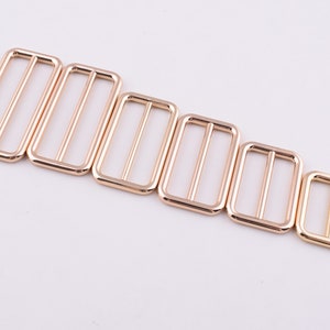 May include: Set of six gold-toned metal slider buckles in various sizes. The buckles are rectangular with a smooth finish.