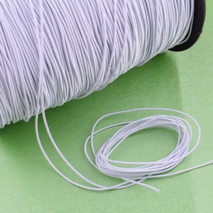 May include: A spool of white elastic cord, with a length of cord lying on a green surface.