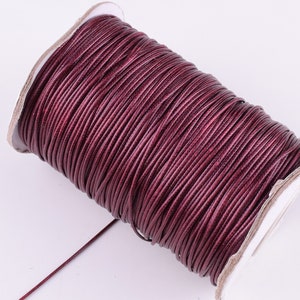 May include: A spool of burgundy waxed cord, a type of string used for jewelry making and crafts.