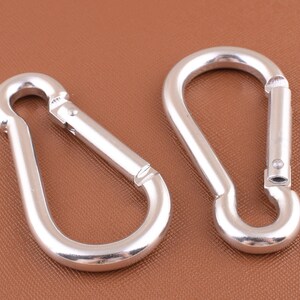 May include: Two silver metal snap hooks with a D-ring opening. The hooks are made of a shiny metal and have a smooth finish.