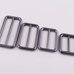 May include: Four silver-toned metal slider buckles of different sizes. The buckles are rectangular with a smooth finish.