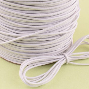 May include: A spool of white elastic cord. The cord is wound tightly around the spool and a length of cord is hanging off the spool.