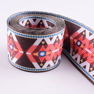 May include: A brown, white, red, and blue patterned webbing with a geometric design. The webbing is rolled up and ready to be used for crafting projects.