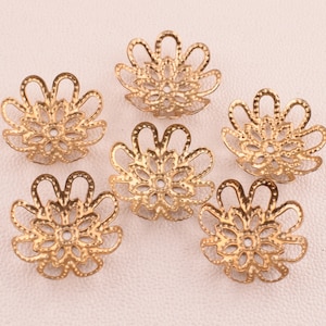 May include: Six gold-colored filigree flower-shaped bead caps. Each cap has a detailed openwork design with a central hole and petal-like edges. These decorative components are ideal for jewelry making and crafting projects.