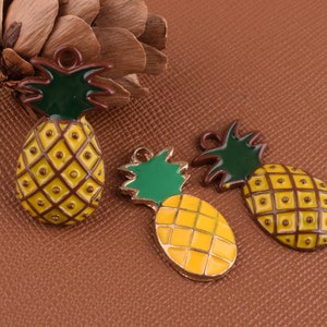 May include: Three gold pineapple charms with green leaves. The pineapples are yellow and brown with a textured surface.