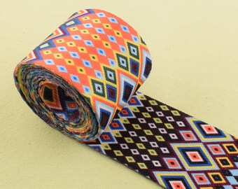 May include: A rolled up colorful patterned webbing with a geometric design in shades of orange, blue, yellow, black, and white.