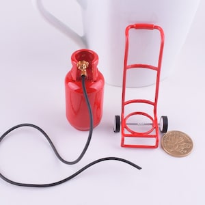 May include: A red miniature propane tank with a black hose and a red metal dolly with two wheels. The dolly has a handle and a metal frame.