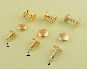Può includere: Assortimento di rivetti, borchie e occhielli in metallo dorato. I rivetti sono di diverse dimensioni e forme, alcuni con testa piatta e altri con testa rotonda. Le borchie sono anche di diverse dimensioni e forme, alcune con testa piatta e altre con testa rotonda. Gli occhielli sono tutti rotondi e hanno un foro al centro.