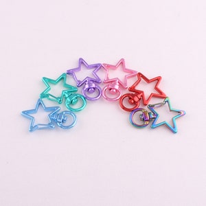 May include: A set of six star-shaped metal keyrings in a rainbow of colours, including teal, purple, pink, red, and blue. Each keyring has a swiveling metal ring.