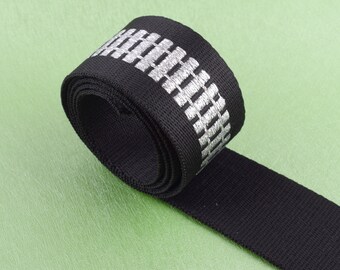 May include: Black webbing with a silver reflective stripe. The stripe has a repeating pattern of small rectangles.
