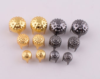 May include: Assortment of gold and silver metal studs with a textured, domed top and three prongs on the bottom.