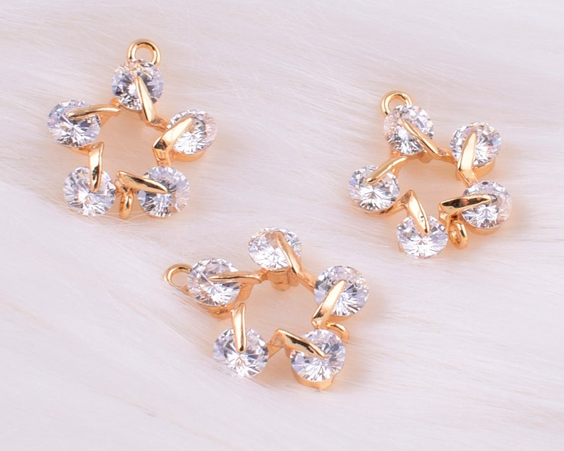 May include: Three gold-tone star-shaped charms with clear crystal accents. Each charm has five points and a loop for attaching to a necklace or bracelet.