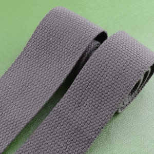 May include: Two rolls of dark gray cotton webbing, a type of fabric used for straps and belts.