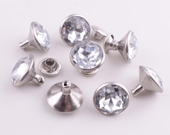 May include: Eight silver-toned, crystal-embellished, decorative knobs with a round, faceted crystal center. The knobs have a flat base and a raised, rounded top.