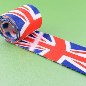 May include: Rolled-up fabric featuring the Union Jack flag design in red, white, and blue. The fabric is unrolled on a light green surface, showcasing the iconic British flag pattern. The material appears to be a sturdy woven fabric.