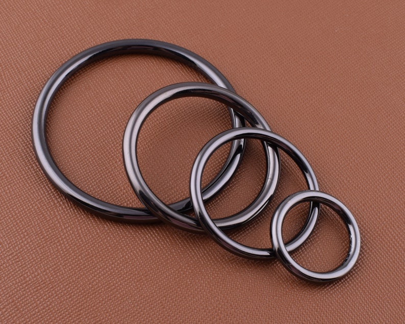 K&ouml;nnte beinhalten: Vier schwarze Metallringe in verschiedenen Gr&ouml;&szlig;en, ineinander verschachtelt. Die Ringe sind glatt und haben eine polierte Oberfl&auml;che.