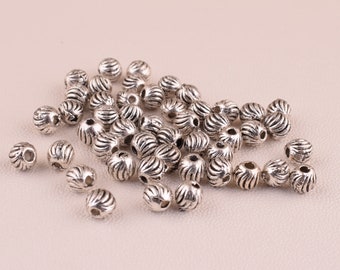 May include: A large pile of silver metal beads with a textured, ridged surface. The beads are round and have a hole in the center for stringing.
