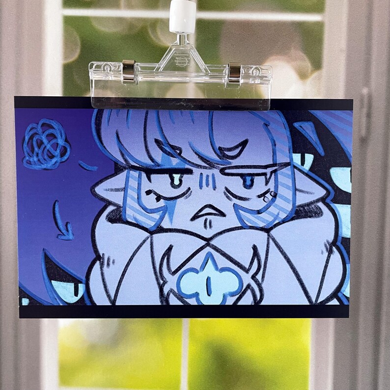 May include: A blue illustration of a character with a stern expression, held by a clear clip. The character has blue hair and is surrounded by shadowy figures with glowing eyes. The artwork is displayed against a window.