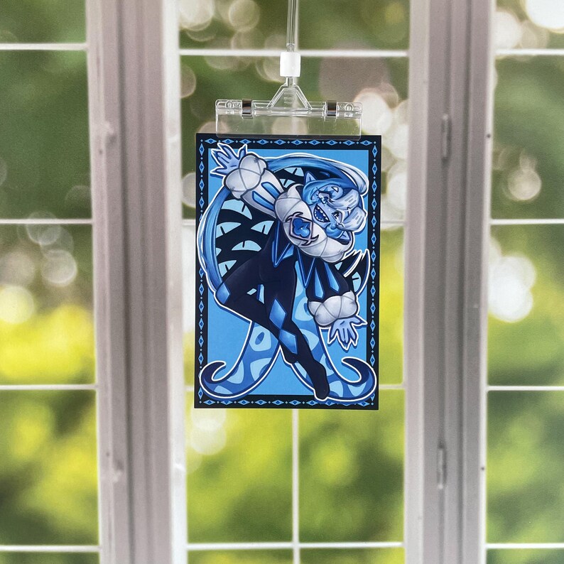 May include: An illustration of a character in blue and black, with a white collar and hat, and long blue hair. The character is in a dynamic pose, set against a light blue background with a decorative border. The image is held by a clear clip.