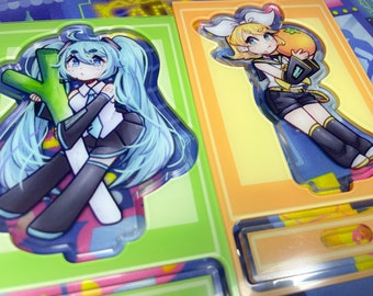 May include: Two colorful anime character illustrations printed on clear acrylic. The illustrations are framed in green and orange borders. The characters are holding a green vegetable and an orange fruit.