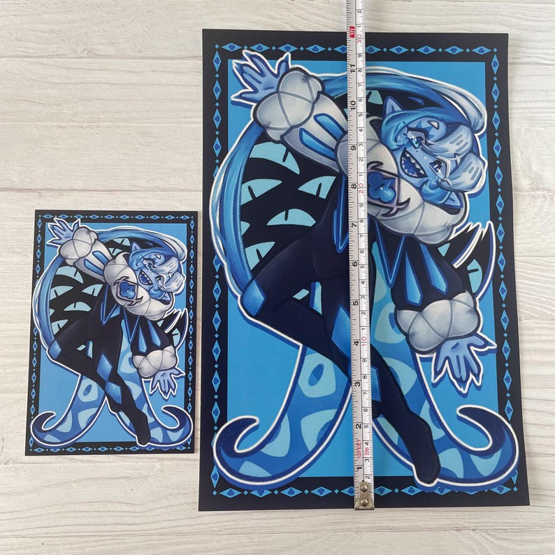 May include: Two art prints featuring a blue and white cartoon character with a mischievous expression. The larger print is approximately 28 cm tall. The character is dressed in a dark blue outfit with white accents and a diamond pattern.