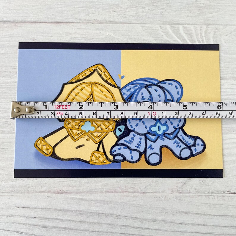 May include: A postcard featuring two cartoon characters, one yellow and one blue, with a tape measure across the image. The tape measure shows a length of approximately 5 inches.