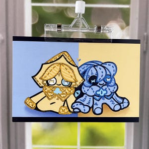 May include: A colorful illustration featuring two cartoon characters. One is yellow with a matching hat and scarf, the other is blue. The background is split, with a blue and yellow section. The artwork is held by a clear clip.