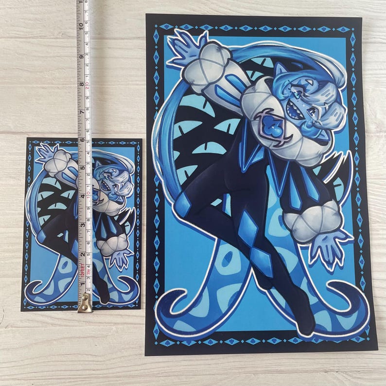 May include: Two art prints featuring a cartoon character in a jester-like outfit. The character is primarily blue and black with white accents. The larger print is approximately 25 cm tall, and the smaller print is about 13 cm tall. Both prints have a blue background.