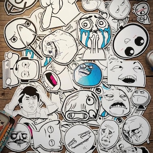 May include: A collection of black and white vinyl stickers featuring various internet meme faces and characters. The assortment includes expressive illustrations, such as crying, laughing, and frustrated figures, with one sticker displaying a rainbow pattern.
