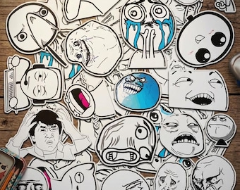 May include: A collection of black and white vinyl stickers featuring various internet meme faces and characters. The assortment includes expressive illustrations, such as crying, laughing, and frustrated figures, with one sticker displaying a rainbow pattern.