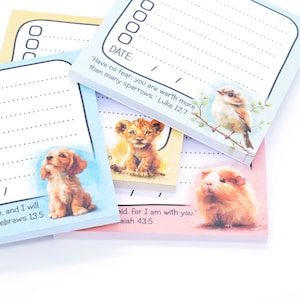May include: A stack of colourful notepads with inspirational quotes and cute animal illustrations. Each notepad features a different animal, including a puppy, a lion cub, a bird, and a guinea pig. The quotes include "Have no fear: you are worth more than many sparrows." Luke 12:7, "...and I will be with you." Hebrews 13:5, and "...for I am with you." Isaiah 43:5.