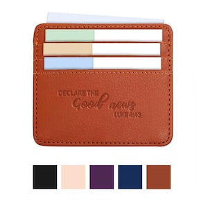 May include: A brown leather card holder with the text "DECLARE THE Good news LUKE 4:43". The card holder has three card slots with colourful cards inside. The card holder is rectangular and has a stitched border.