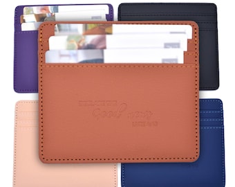 May include: A collection of five rectangular card holders in purple, black, tan, light pink, and blue. The tan card holder in the centre features the embossed text "DECLARE THE Good news LUKE 4:43" and contains white cards in its slots.