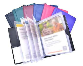May include: A collection of rectangular card holders in various colors including black, teal, maroon, blue, pink, and purple. Each holder features clear plastic interior sleeves designed to display cards, with one open holder showing blurred text and imagery.