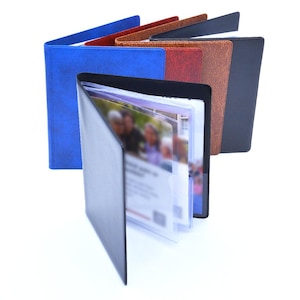 May include: A collection of five menu covers or document holders arranged in a fan shape. The covers feature textured finishes in blue, red, brown, and black. Each holder contains clear plastic sleeves for displaying inserts or menus.