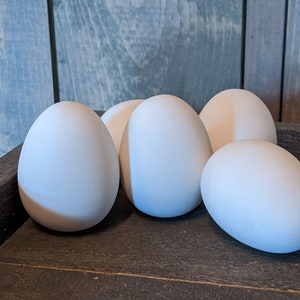 May include: Five white eggs arranged on a wooden surface. The eggs are smooth and oval-shaped.