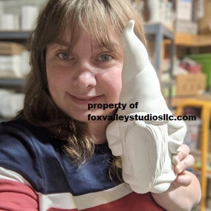 May include: A white ceramic gnome figurine with a long pointed hat. The gnome is holding a sign that says "property of foxvalleystudiosllc.com".