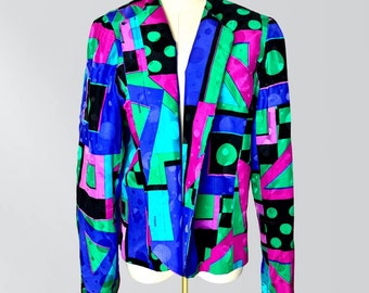 May include: A vibrant, patterned blazer in a kaleidoscope of colors. The jacket features a bold geometric design with black, green, blue, pink, and purple shapes. The open front and long sleeves create a striking visual statement. The blazer is displayed on a mannequin.