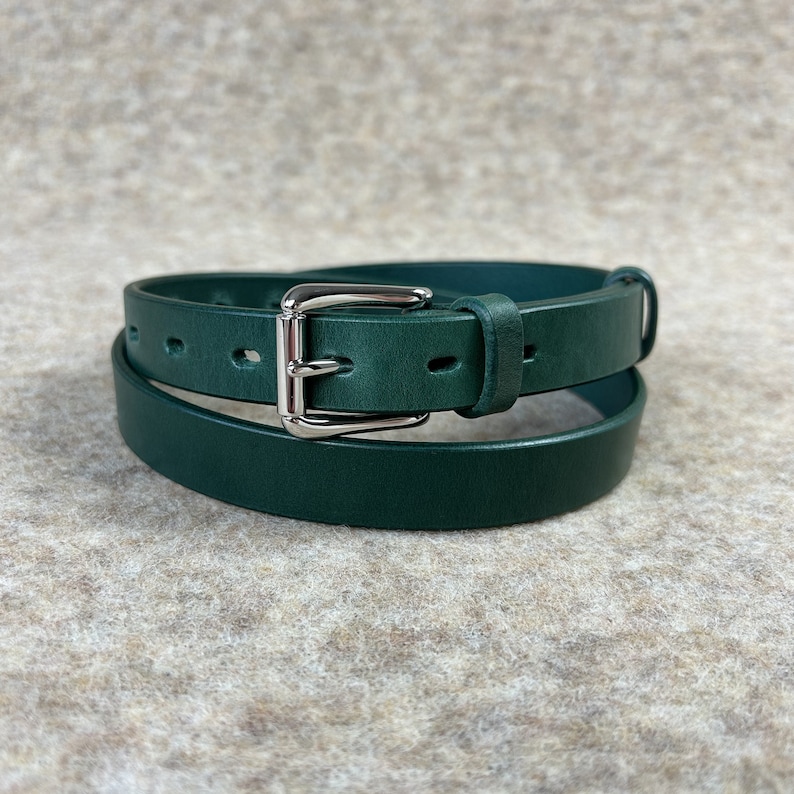 May include: A dark green leather belt with a silver buckle. The belt is folded in half and the buckle is visible.