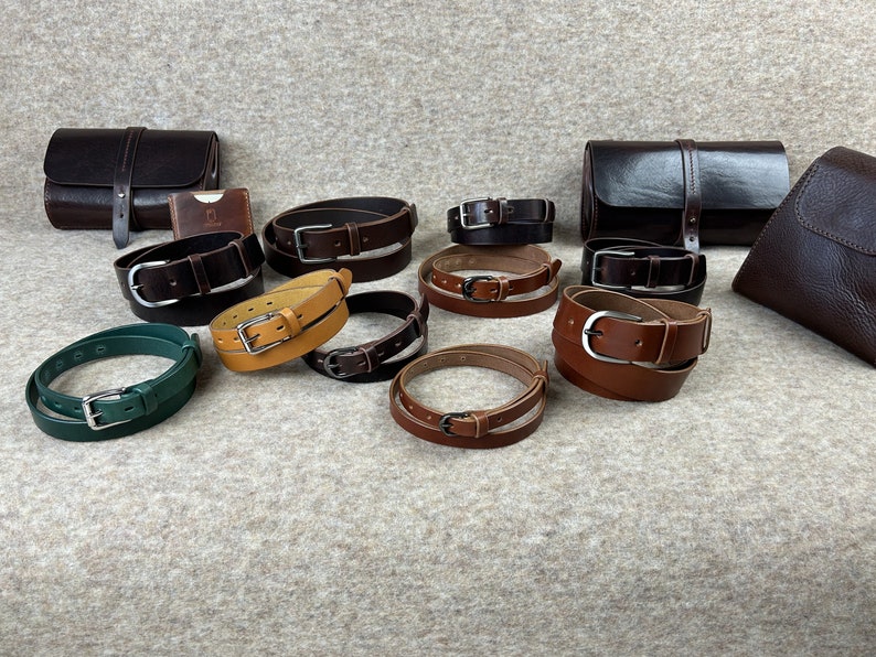 May include: A collection of leather belts in various colors, including brown, tan, green, and black. The belts are arranged in a circle on a light brown surface.