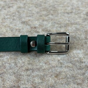 May include: A dark green leather belt with a silver buckle. The buckle has a double prong design.