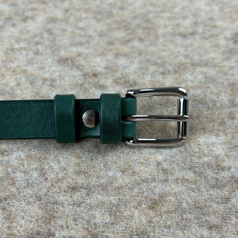 May include: A dark green leather belt with a silver buckle. The buckle has a double prong design.