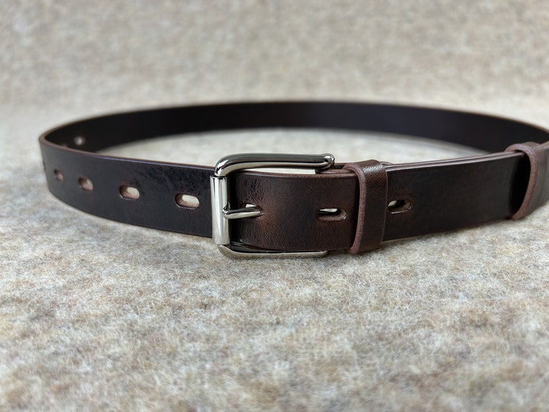 May include: A brown leather belt with a silver buckle. The belt has five evenly spaced holes for adjusting the fit.