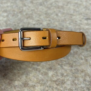 May include: A brown leather belt with a silver buckle. The belt is folded in half and the buckle is in the center of the image.