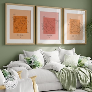 Puede incluir: Tres impresiones artísticas enmarcadas con personajes de Pokémon. Cada impresión presenta un dibujo lineal minimalista de un Pokémon sobre un fondo de color, con texto japonés debajo. Los marcos son de madera clara y las impresiones se exhiben sobre un sofá blanco.