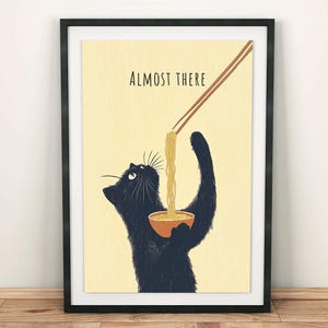 Könnte beinhalten: Gerahmter Kunstdruck mit einer schwarzen Katze, die nach Nudeln aus einer Schüssel greift. Der Text "ALMOST THERE" steht über der Katze. Der Hintergrund ist hellgelb.