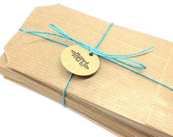 Può includere: Un mucchio di sacchetti di carta marrone legati insieme con uno spago blu turchese e un'etichetta rotonda marrone su cui è scritto "Merci" in lettere nere.