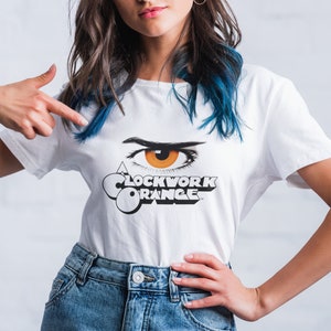 K&ouml;nnte beinhalten: Wei&szlig;es T-Shirt mit einer schwarz-wei&szlig;en Grafik eines Auges mit orangefarbener Iris und dem Text "A Clockwork Orange".